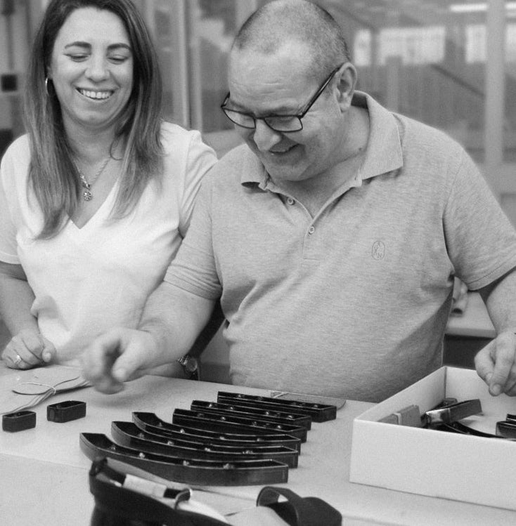 A black and white photo showing a man and a woman standing at a table, looking at and handling small dark molded plastic components in a box.